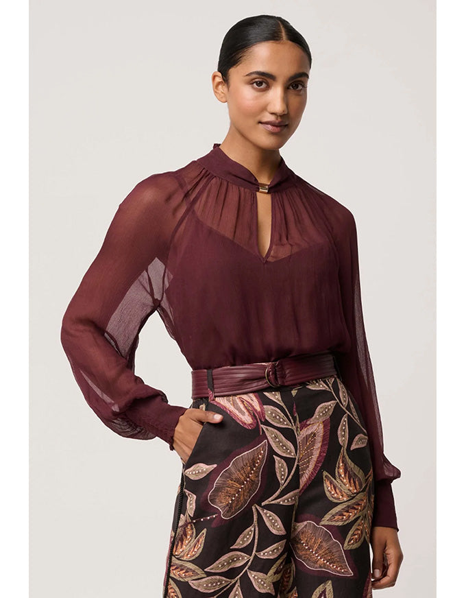 Woman wearing a burgundy sheer blouse with patterned pants on a white background