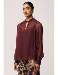 Woman wearing a sheer burgundy blouse with a plain background