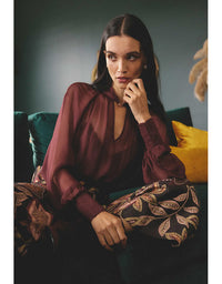 Woman in a burgundy top and patterned pants sitting on a couch.
