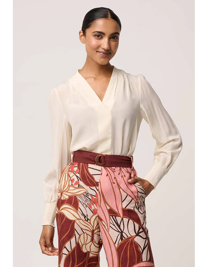 Woman wearing a white blouse and patterned pants with a belt against a light background