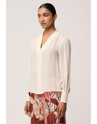 Woman wearing a cream blouse with a plain background