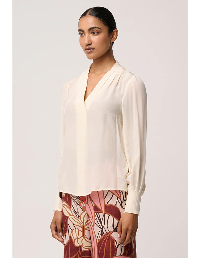 Woman wearing a cream blouse with a plain background