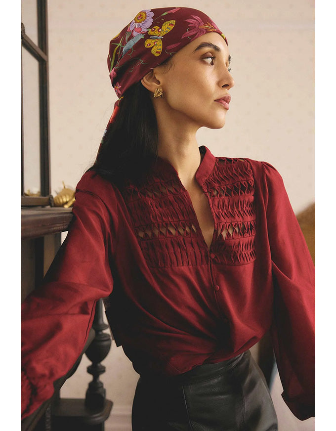 Woman wearing a red embroidered blouse and headscarf with floral patterns.