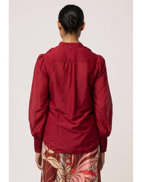 Person wearing a red blouse with floral pants on a plain background