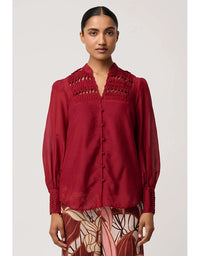 Woman wearing a red blouse with intricate collar design on a plain background