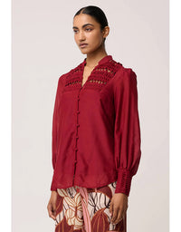 Woman wearing a red blouse with intricate detailing on a plain background