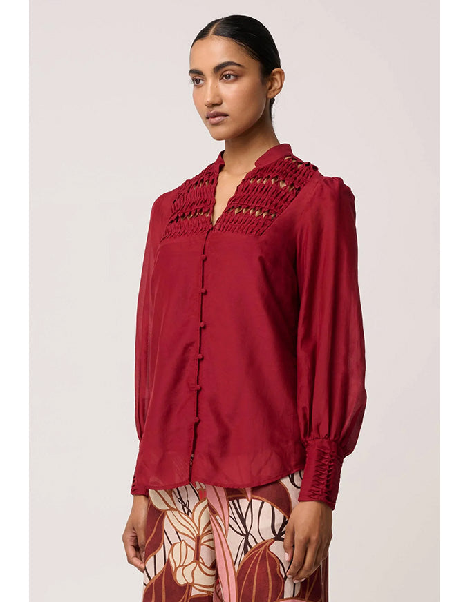Woman wearing a red blouse with intricate detailing on a plain background