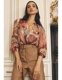 Woman wearing a patterned blouse and beige pants in an elegant interior setting.