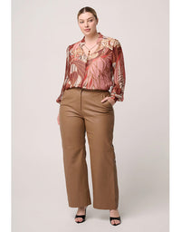 Woman wearing a patterned blouse and brown pants on a plain background
