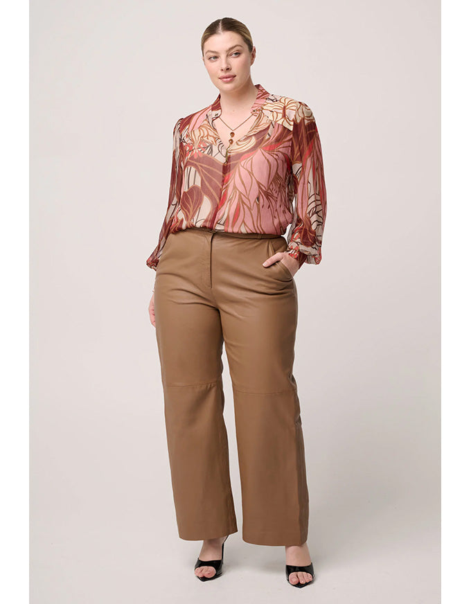 Woman wearing a patterned blouse and brown pants on a plain background