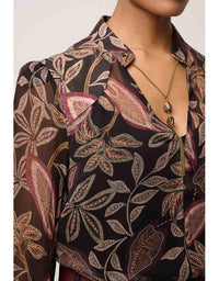 Woman wearing a dark floral patterned blouse with a necklace against a neutral background