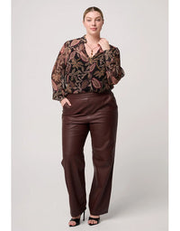 Woman wearing a patterned blouse and brown pants on a white background