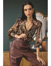 Woman wearing a patterned blouse and brown pants in an indoor setting