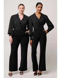 Two women wearing black jumpsuits with embellished details on a white background