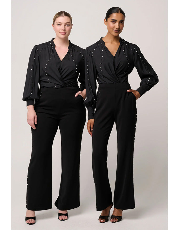Two women wearing black jumpsuits with embellished details on a white background