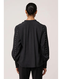 Black blouse with pearl embellishments on sleeves worn by a person against a plain background