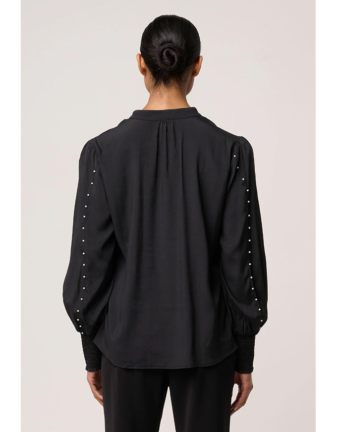 Black blouse with pearl embellishments on sleeves worn by a person against a plain background