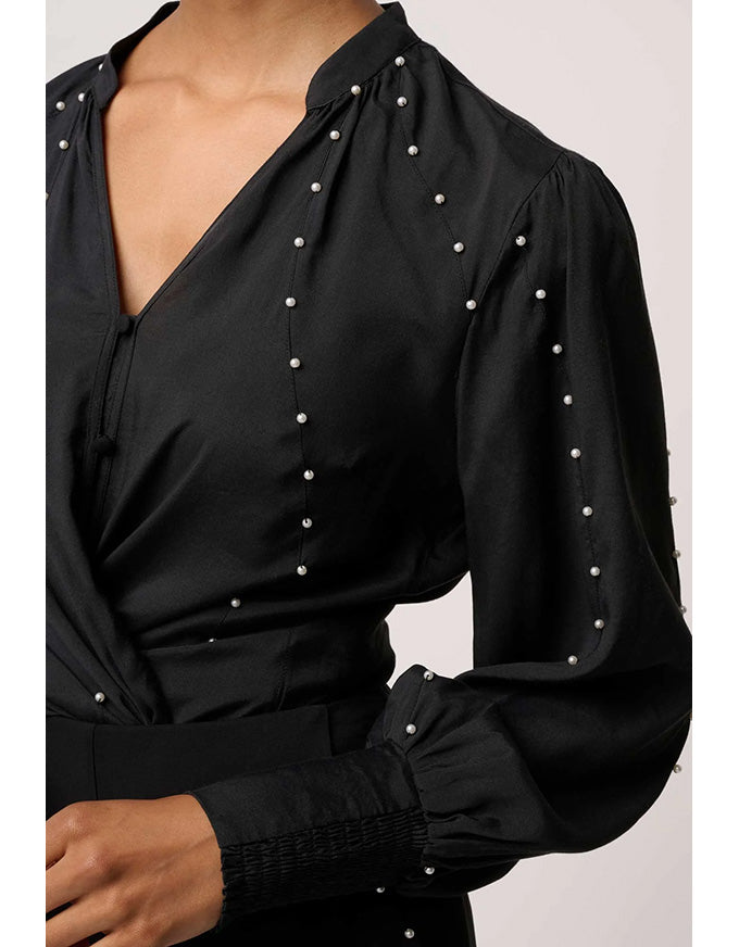 Black blouse with pearl embellishments on a plain background