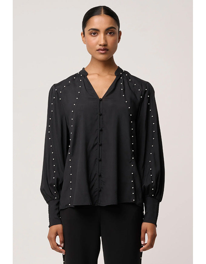 Woman wearing a black blouse with pearl embellishments on a plain background
