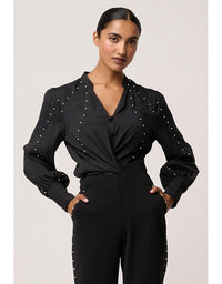 Woman wearing a black outfit with pearl embellishments on a plain background