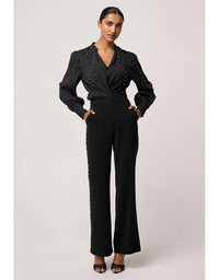 Woman wearing a black jumpsuit with embellishments on a light gray background