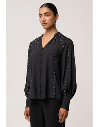 Woman wearing a black blouse with pearl embellishments on a plain background