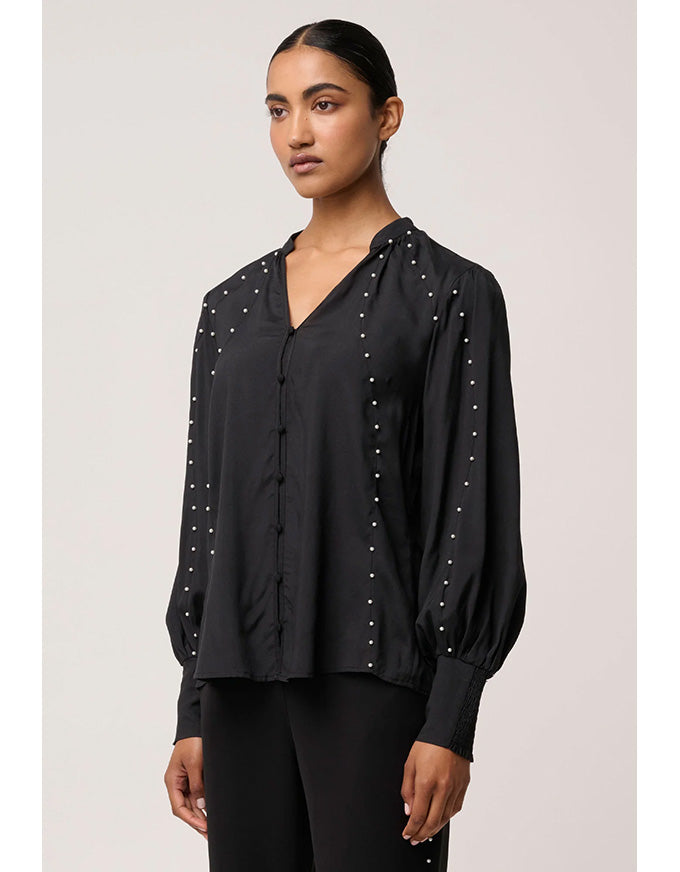 Woman wearing a black blouse with pearl embellishments on a plain background
