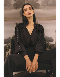 Woman wearing a black outfit with pearl embellishments against a scenic background