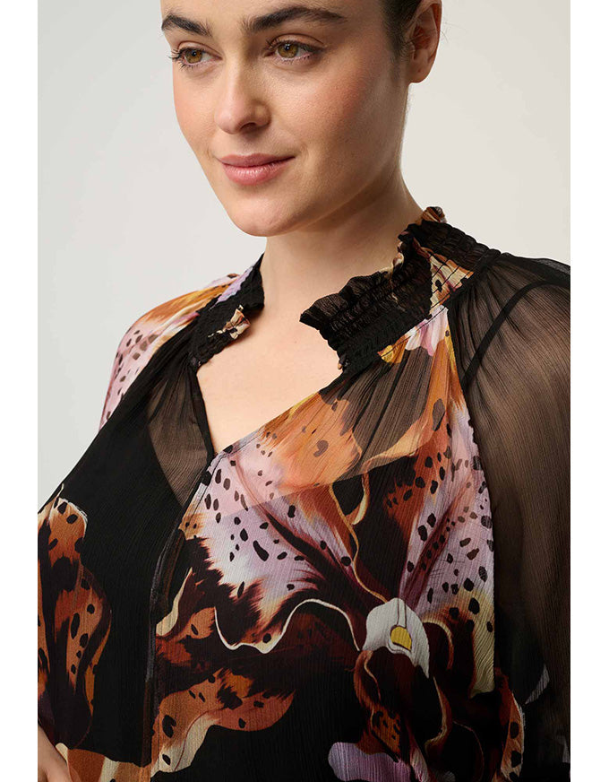 A close-up of a woman wearing a sheer black mesh top layered over a floral and leopard-print blouse with orange, brown, black, and white tones.