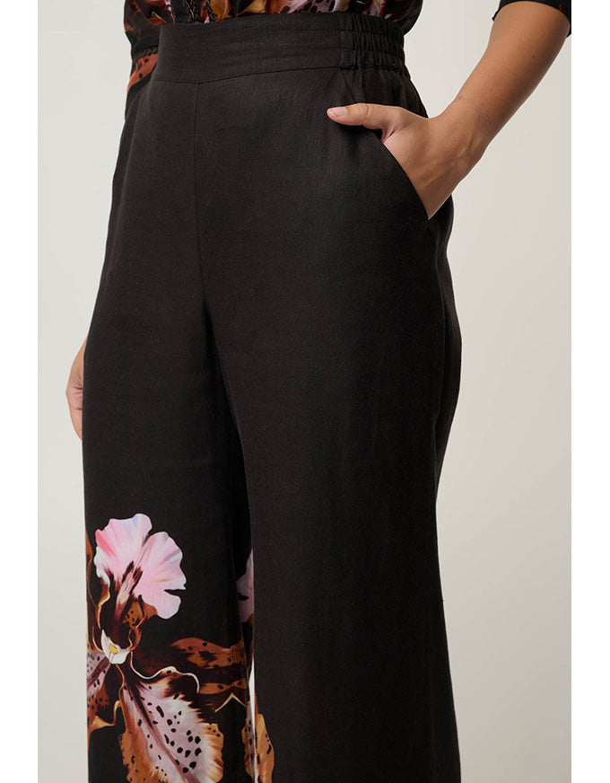 Black wide-leg trousers with a pink and brown floral print near the lower left leg, shown on a model against a light gray background.