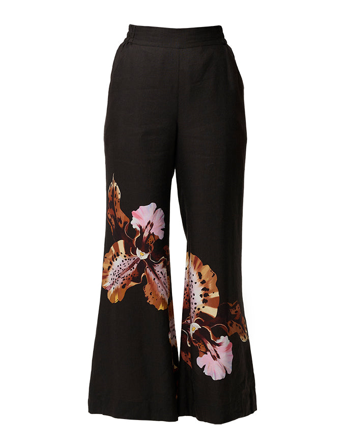 Black wide-leg pants featuring large brown, pink, and white floral orchid prints on the lower legs, shown against a plain white background.