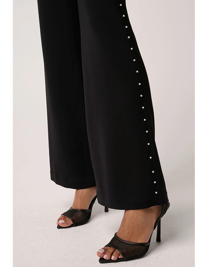 Black pants with button details worn by a person on a plain background