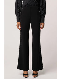 Black pants with decorative elements worn by a person on a light gray background