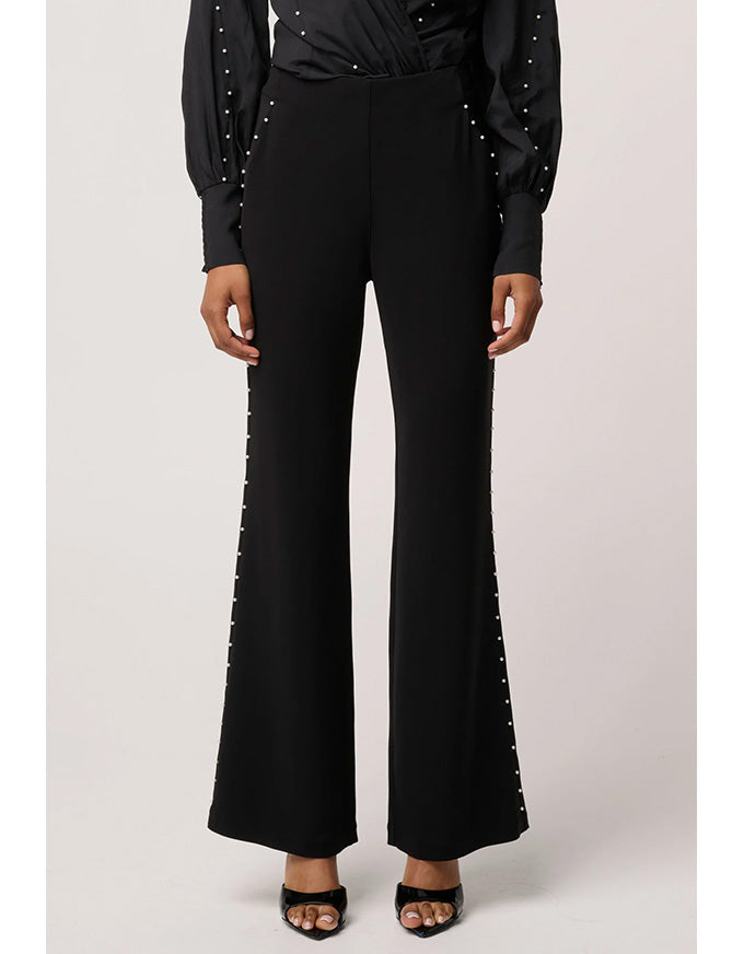 Black pants with decorative elements worn by a person on a light gray background