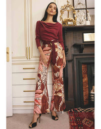 Woman in a burgundy top and patterned pants standing in a room with decorative elements.