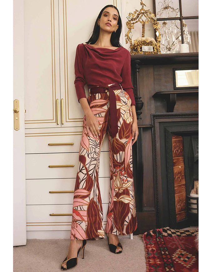 Woman in a burgundy top and patterned pants standing in a room with decorative elements.
