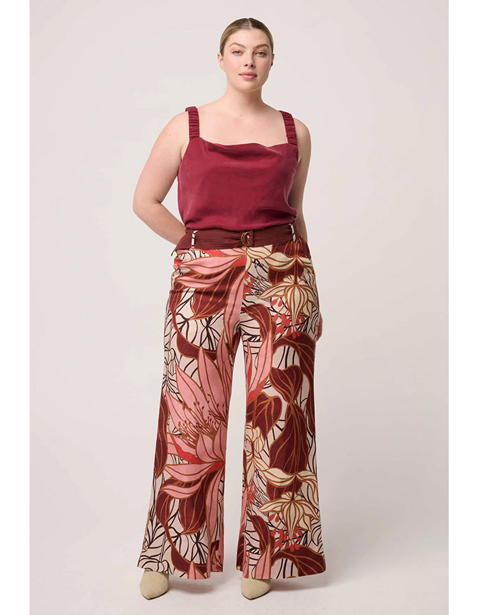 Woman wearing a burgundy top and patterned pants on a light background