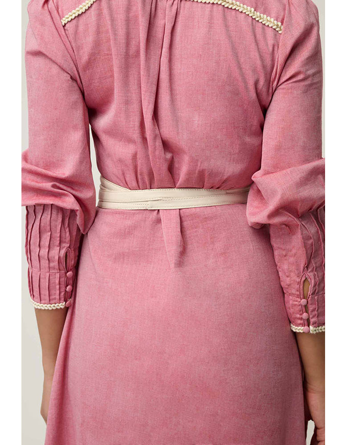A close-up of a dusty pink dress with three-quarter sleeves, featuring cream-colored beaded trim along the shoulders and cuffs, and a matching cream waist belt.