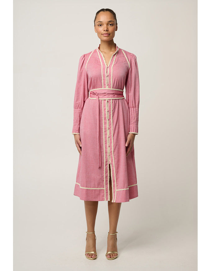 A woman modeling a pink long-sleeve midi dress with cream-colored trim and a matching tie belt, standing against a neutral light beige studio background.