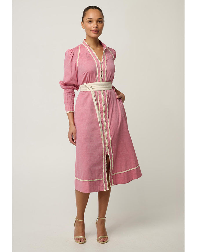 A woman modeling a pink long-sleeve midi dress with cream-colored trim and a matching cream belt, standing against a light gray studio background.