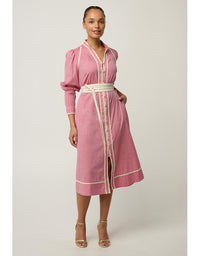 A woman modeling a pink long-sleeve midi dress with cream-colored trim and a matching cream belt, standing against a light gray studio background.
