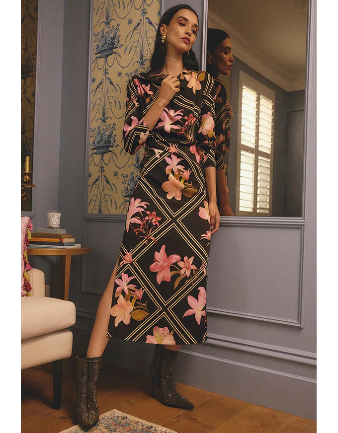 Woman in a floral dress standing in a room with patterned wallpaper.