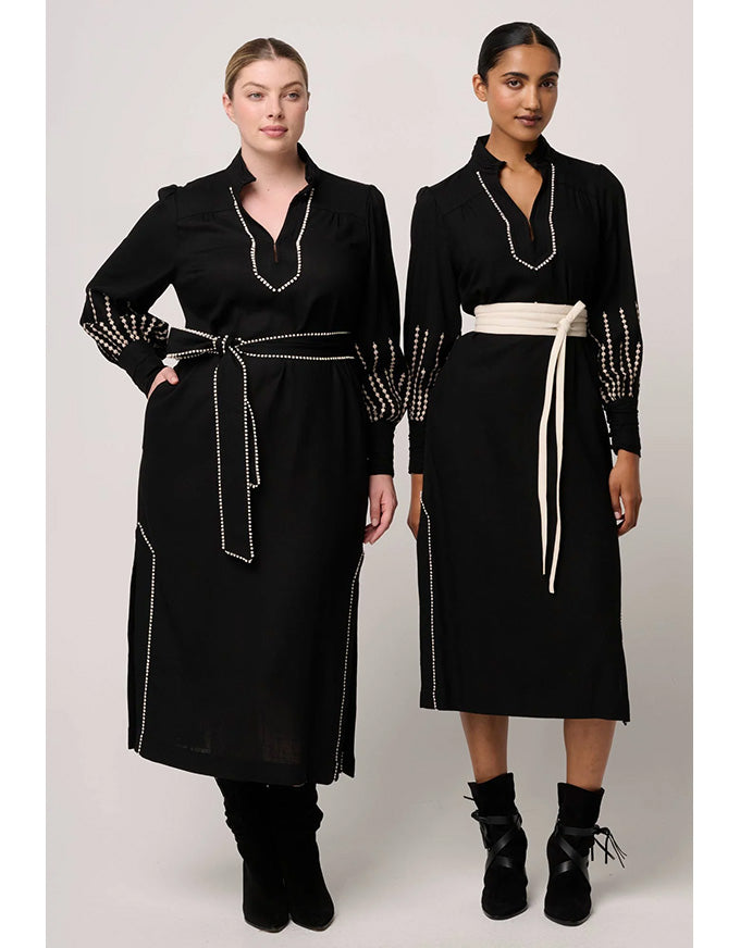 Two women wearing black dresses with white trim on a plain background