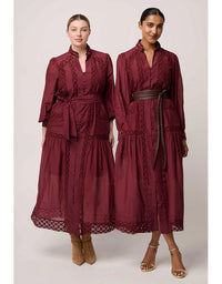 Two women wearing burgundy dresses with lace details on a plain background