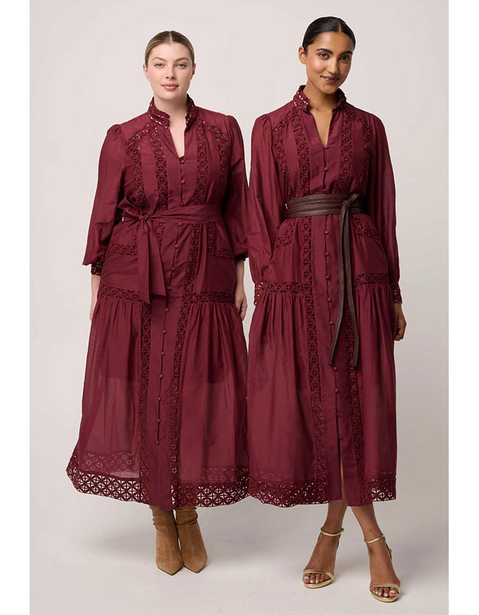Two women wearing burgundy dresses with lace details on a plain background