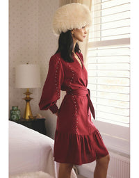 Woman in a red dress and fur hat standing in a bedroom.