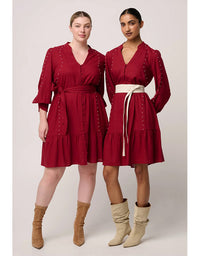 Two women wearing red dresses with long sleeves and a belt, standing side by side against a plain background.