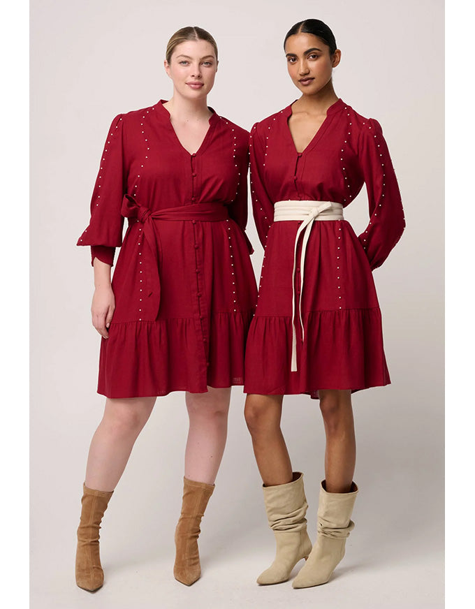 Two women wearing red dresses with long sleeves and a belt, standing side by side against a plain background.