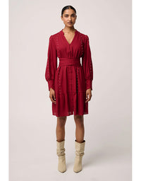 Woman wearing a red dress with long sleeves and beige boots on a light gray background