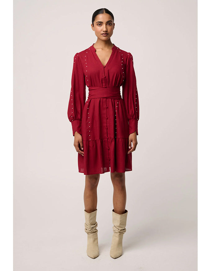 Woman wearing a red dress with long sleeves and beige boots on a light gray background